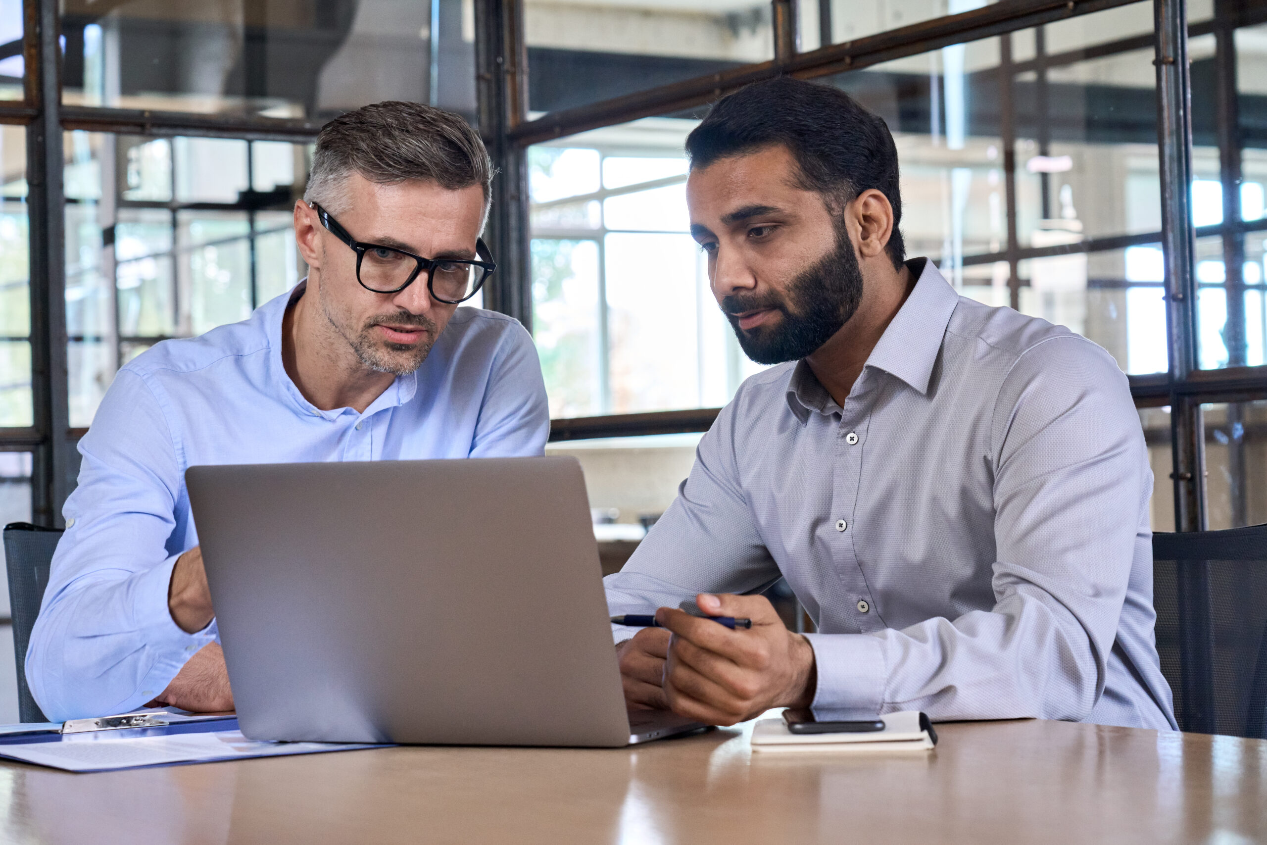 2 hommes discutent, assis à un bureau, derrière un ordinateur portable