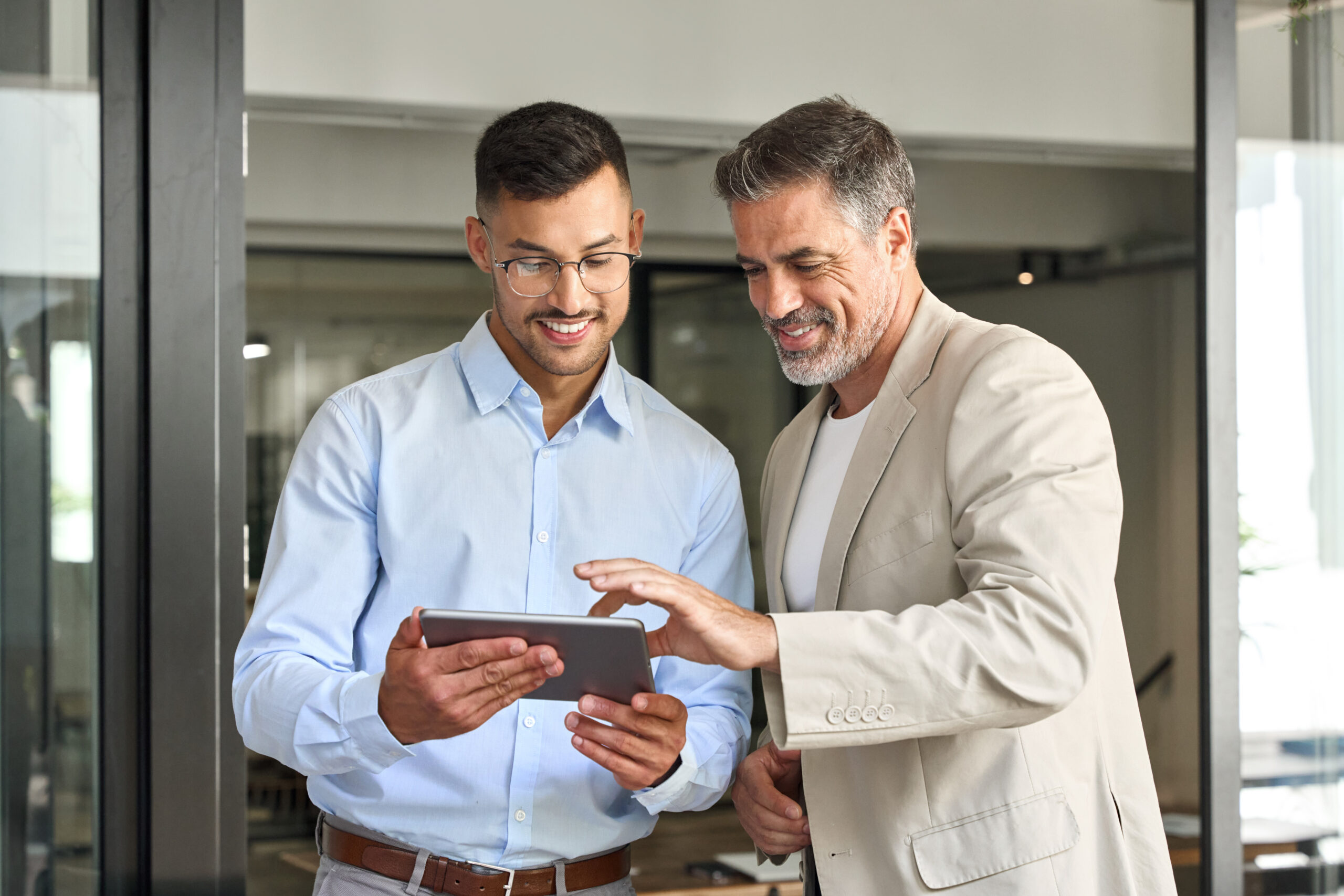 Équipe de deux hommes d'affaires heureux travaillant debout au bureau à l'aide d'une tablette numérique pour réfléchir à une offre de services